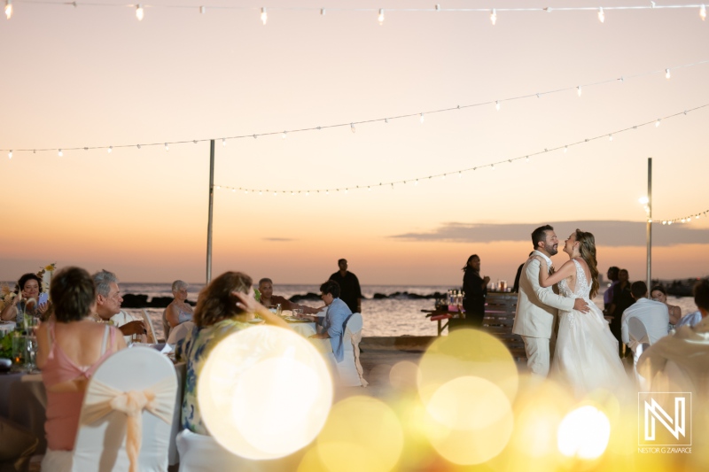 A romantic sunset wedding ceremony by the beach with guests celebrating the couple\'s first dance under fairy lights on a beautiful evening