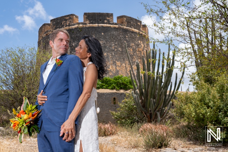 Wedding celebration at Fort Beekenburg, Curacao, featuring a couple with a beautiful backdrop and vibrant floral arrangements in the sunny outdoor setting