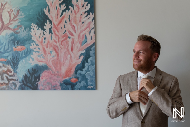 Groom adjusting his tie in a coral-themed setting before the wedding ceremony in Curacao