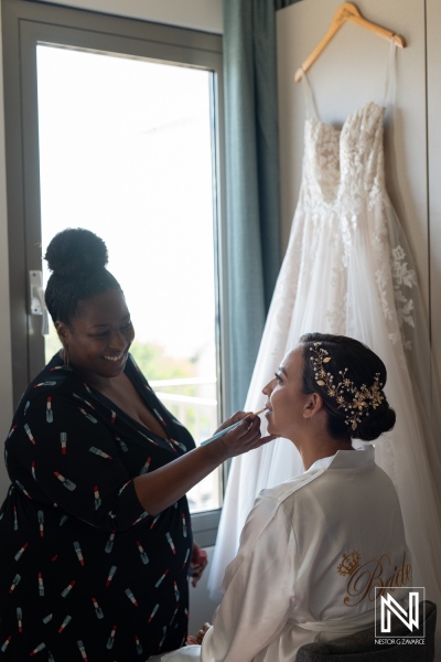 Bride prepares for wedding in beautiful Curacao setting with makeup artist enhancing her look amid elegant dress