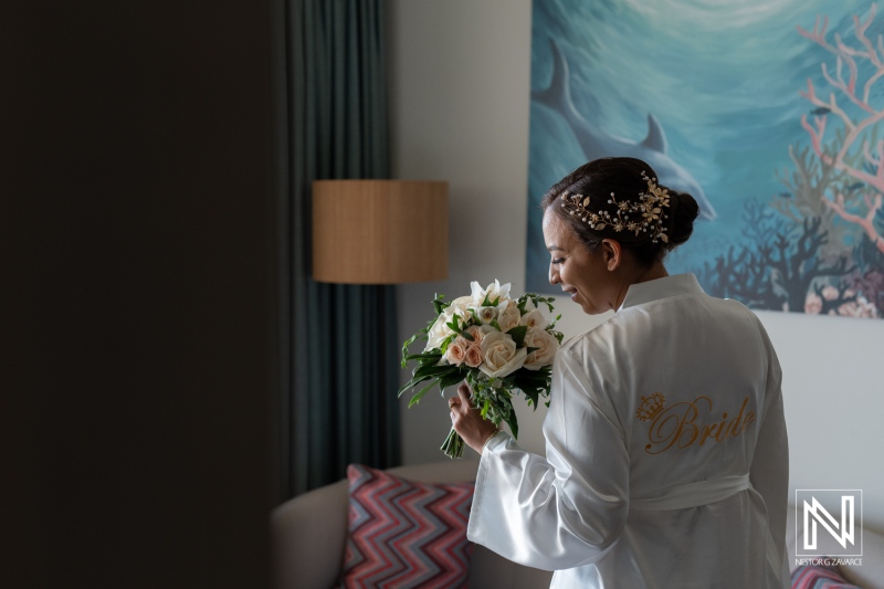 Bride preparing for her wedding in Curacao with a beautiful bouquet in hand and a robe adorned with the word bride