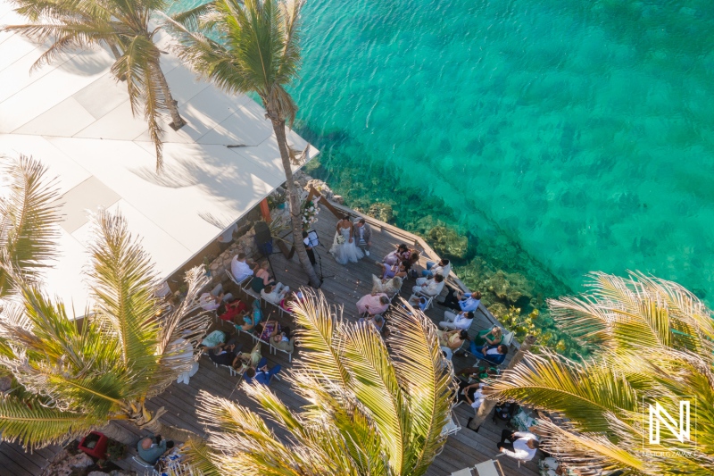 Wedding ceremony in Curacao by the crystal-clear waters surrounded by palm trees and guests enjoying the celebration