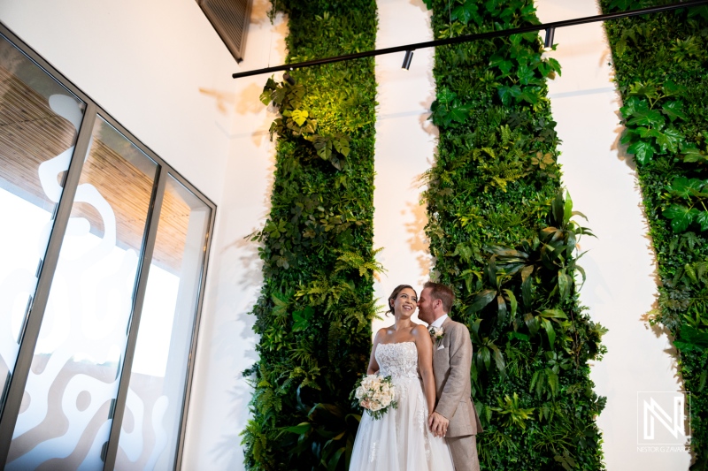 Wedding couple poses in front of lush green wall at a beautiful venue in Curacao during their special day